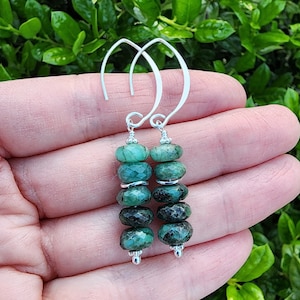 May include: A pair of silver dangle earrings with green gemstone beads. The earrings have a simple hoop design and feature multiple round beads.