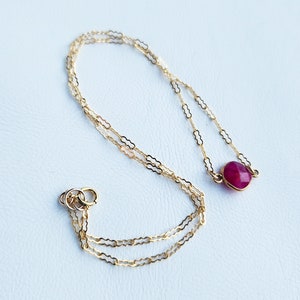 May include: A delicate gold chain necklace with a single round red gemstone pendant.