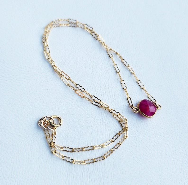 May include: A delicate gold chain necklace with a single round red gemstone pendant.