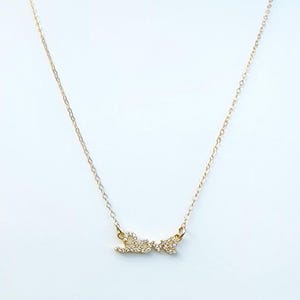 May include: A delicate gold-colored necklace with the word "Love" spelled out in cursive. The letters are embellished with small, sparkling crystals. The necklace hangs on a fine chain against a white background.