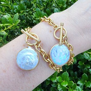 May include: A gold chain bracelet with two pearl charms. One charm is round and the other is teardrop shaped.