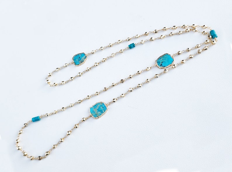 May include: A gold chain necklace with three turquoise stones. The chain is made of small, round beads.