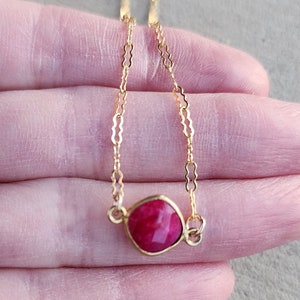 May include: A delicate gold chain necklace with a square-shaped, bright pink gemstone pendant.
