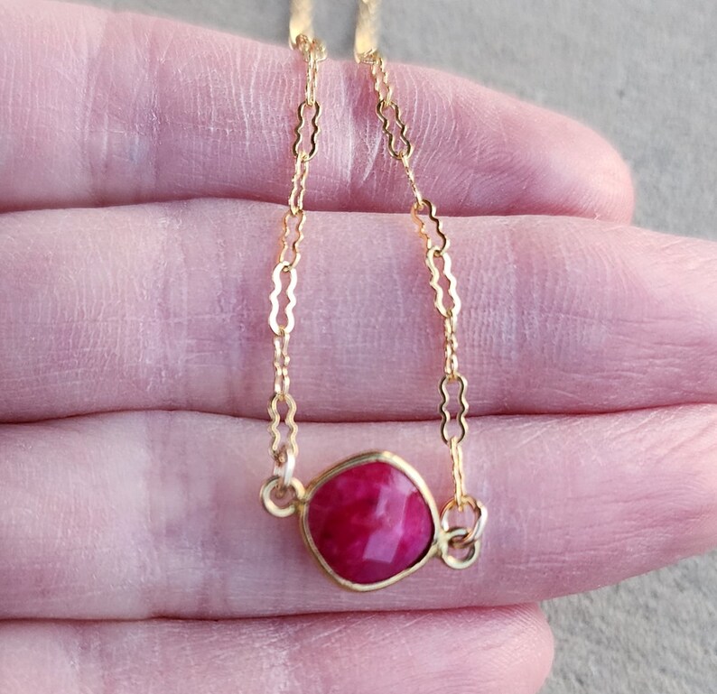 May include: A delicate gold chain necklace with a square-shaped, bright pink gemstone pendant.