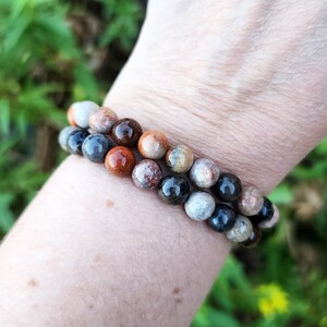 Puede incluir: Dos pulseras hechas de cuentas redondas de colores. Las cuentas son una mezcla de marr&oacute;n, gris y blanco con un patr&oacute;n moteado. Las pulseras se llevan en la mu&ntilde;eca.