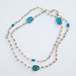 May include: A gold chain necklace with turquoise stones. The necklace is made of small gold beads and has three turquoise stones.