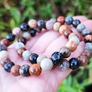 Puede incluir: Dos pulseras hechas de cuentas marrones, negras y blancas. Las cuentas son redondas y tienen un aspecto natural y org&aacute;nico.