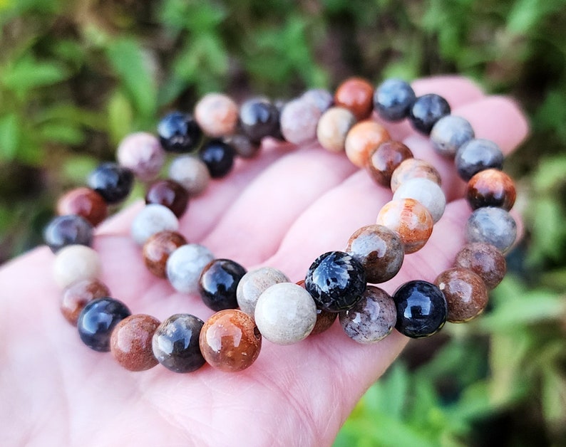 Puede incluir: Dos pulseras hechas de cuentas marrones, negras y blancas. Las cuentas son redondas y tienen un aspecto natural y org&aacute;nico.
