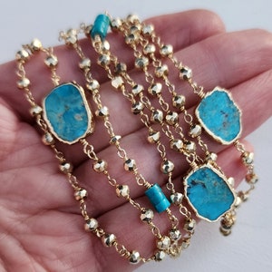 May include: A gold chain necklace with turquoise stones. The chain is made of small, faceted beads. The turquoise stones are irregular in shape and have a blue-green color.