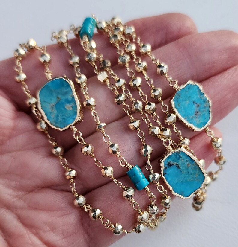 May include: A gold chain necklace with turquoise stones. The chain is made of small, faceted beads. The turquoise stones are irregular in shape and have a blue-green color.