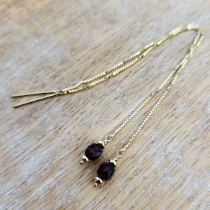 May include: A pair of gold chain earrings with dark red gemstone beads. The earrings are long and dangle.