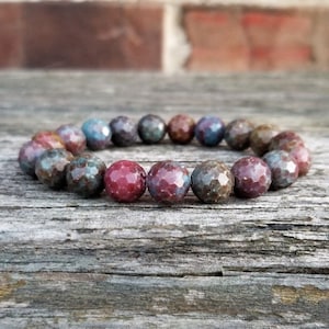 May include: A bracelet made of faceted gemstone beads in shades of red, pink, and blue. The beads are arranged in a circular pattern and have a slightly irregular shape.