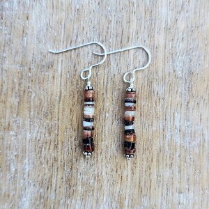 Peut inclure: Une paire de boucles d'oreilles pendantes en argent avec des perles brunes, blanches et noires.