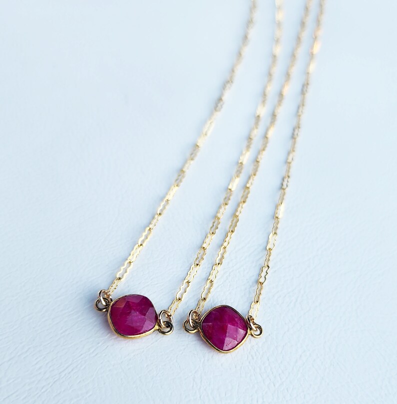 May include: Two delicate gold chains with a ruby gemstone pendant on each. The ruby gemstones are faceted and have a deep red color.
