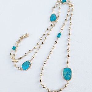 May include: A gold chain necklace with turquoise stones. The necklace is made of small, round beads and features three larger turquoise stones.