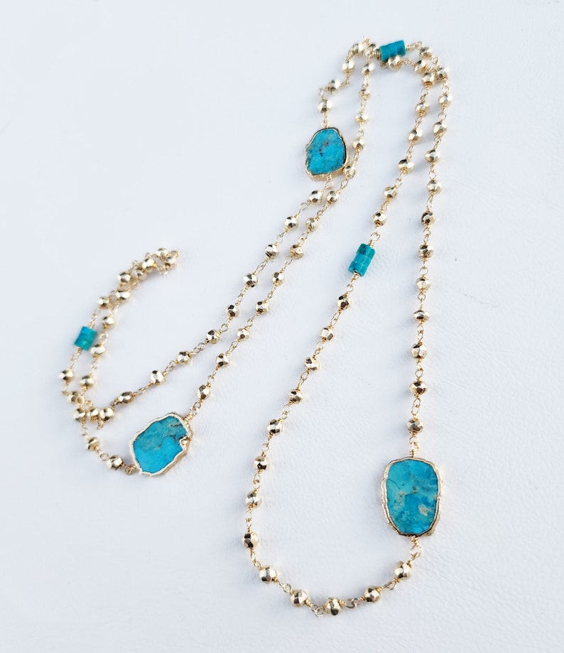 May include: A gold chain necklace with turquoise stones. The necklace is made of small, round beads and features three larger turquoise stones.