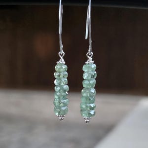 May include: A pair of drop earrings with a string of light green, faceted gemstones on silver-coloured wires. The earrings have a delicate design, with a small decorative element at the base of the gemstone strand.