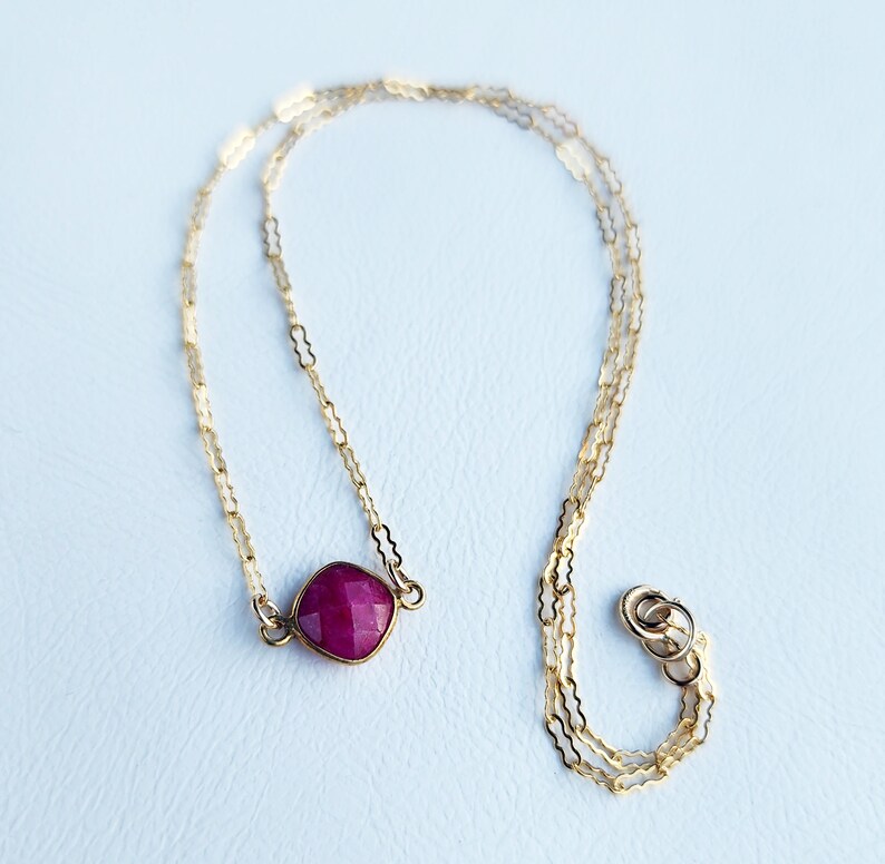 May include: A delicate gold chain necklace with a square-shaped ruby gemstone pendant.