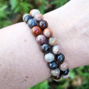 Puede incluir: Un brazalete hecho de piedras marrones, negras y blancas. Las piedras son redondas y tienen un aspecto natural y sin pulir.