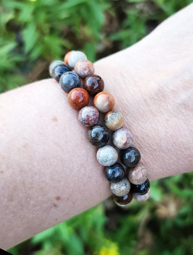 Puede incluir: Un brazalete hecho de piedras marrones, negras y blancas. Las piedras son redondas y tienen un aspecto natural y sin pulir.
