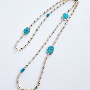 May include: A gold chain necklace with turquoise stones. The necklace is made of small, round beads and has a long, flowing design.