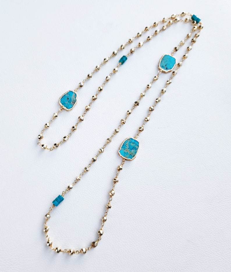 May include: A gold chain necklace with turquoise stones. The necklace is made of small, round beads and has a long, flowing design.