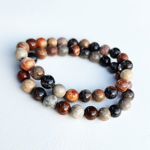 Puede incluir: Un brazalete de cuentas multicolores con cuentas marrones, negras y naranjas. El brazalete est&aacute; hecho de piedra natural y tiene un aspecto r&uacute;stico.