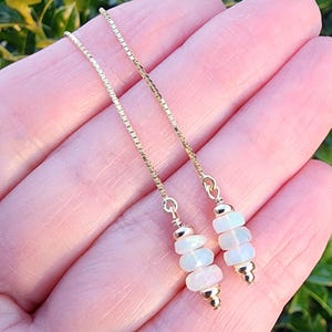 May include: A pair of gold chain earrings with three white opal beads on each chain.