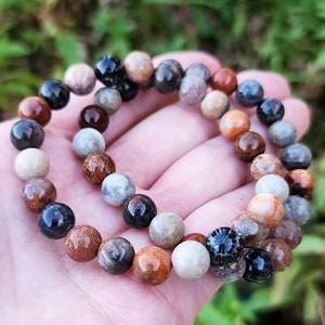Puede incluir: Un brazalete de cuentas multicolores con cuentas marrones, beige, naranja y negras. El brazalete est&aacute; hecho de piedra natural y tiene un aspecto terroso &uacute;nico.