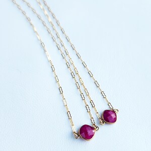 May include: Three gold chains with ruby red gemstone pendants. The chains are made of small, linked ovals.