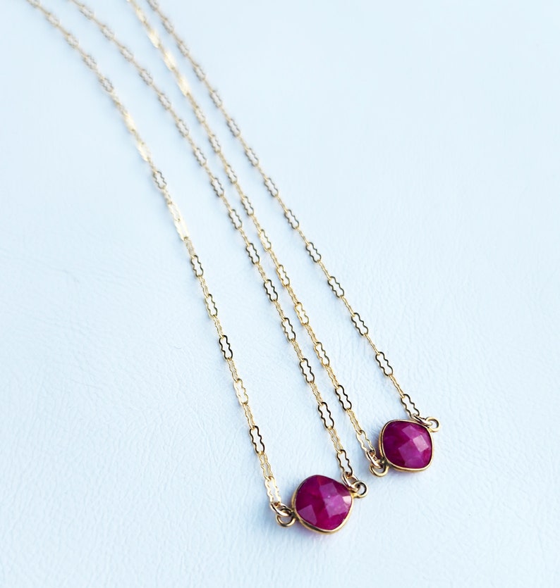 May include: Three gold chains with ruby red gemstone pendants. The chains are made of small, linked ovals.
