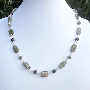 May include: A necklace featuring rectangular and small round beads in shades of sage green, olive, and deep maroon. The beads are connected by thin silver-toned metal links, creating a delicate chain pattern that rests evenly around the neck.