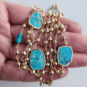 May include: A gold chain necklace with turquoise stones. The chain is made of small, faceted beads and has multiple strands. The turquoise stones are irregular in shape and have a blue-green color.