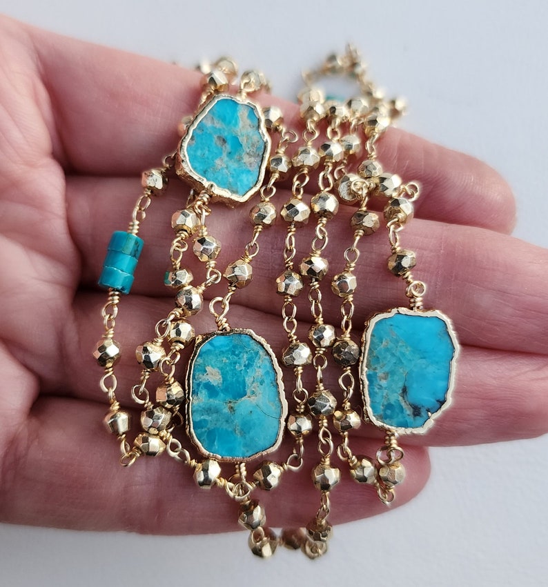 May include: A gold chain necklace with turquoise stones. The chain is made of small, faceted beads and has multiple strands. The turquoise stones are irregular in shape and have a blue-green color.