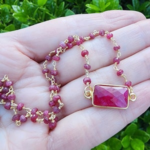 May include: A gold chain necklace with a rectangular ruby pendant. The necklace is made of small ruby beads and gold wire.