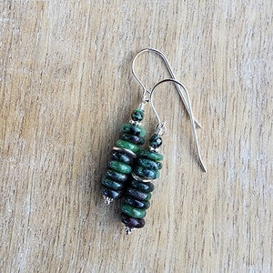 May include: A pair of silver dangle earrings with green and black gemstone beads. The beads are stacked in a graduated pattern, with the largest beads at the bottom.