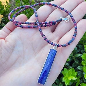 May include: A necklace made of small blue and pink gemstone beads with a long, rectangular blue gemstone pendant.