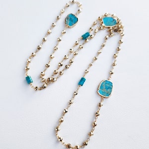 May include: A long gold chain necklace with turquoise stones. The necklace has a layered design with multiple strands of beads.