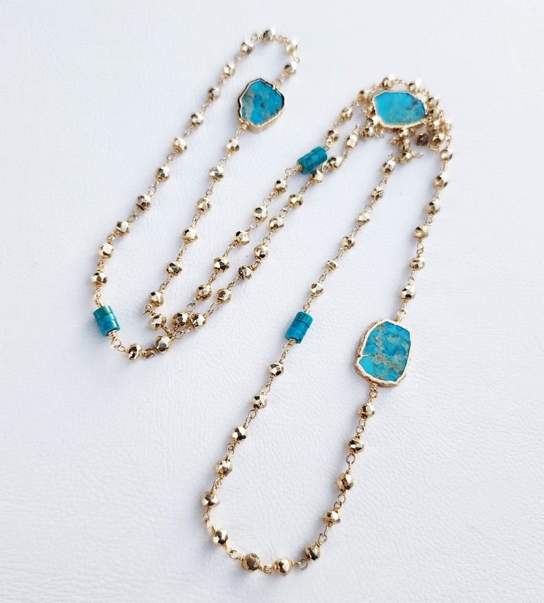 May include: A long gold chain necklace with turquoise stones. The necklace has a layered design with multiple strands of beads.