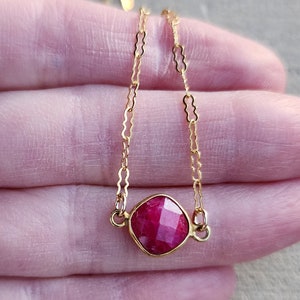 May include: A delicate gold chain necklace with a square-shaped ruby gemstone pendant.