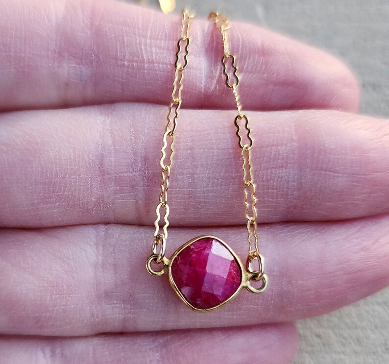 May include: A delicate gold chain necklace with a square-shaped ruby gemstone pendant.
