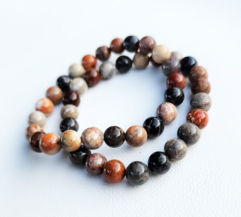 Puede incluir: Un brazalete de doble cadena hecho de cuentas de piedras preciosas marrones, negras y blancas. Las cuentas son redondas y tienen un acabado natural y pulido.
