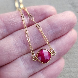May include: A delicate gold chain necklace with a square-shaped ruby gemstone pendant.