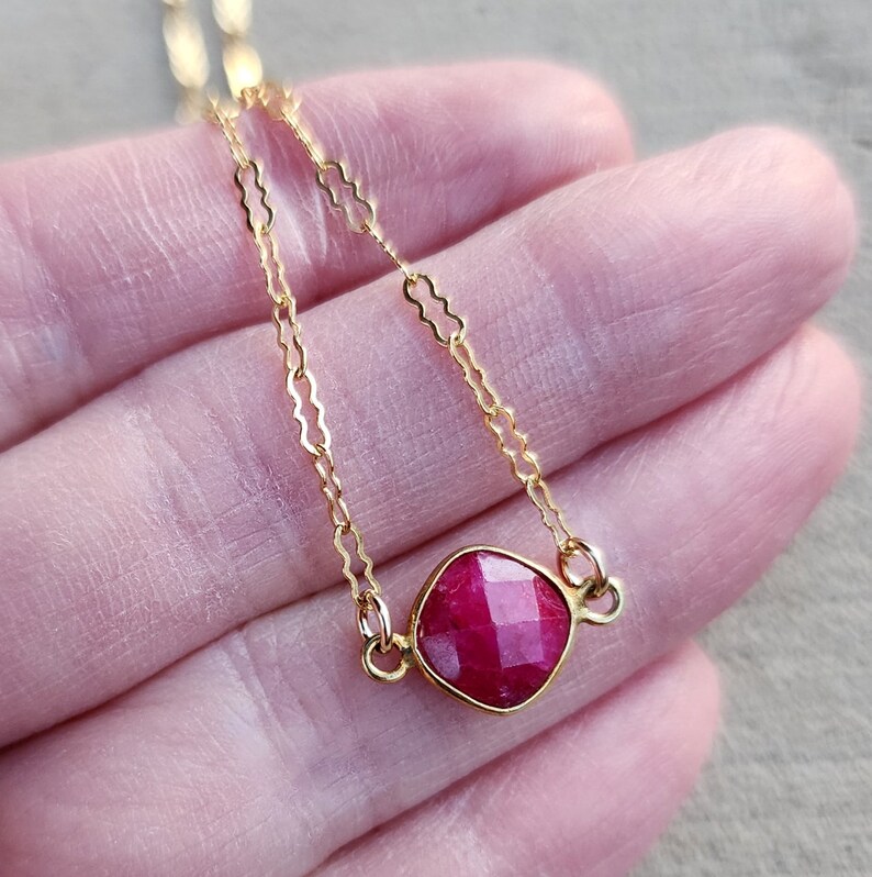 May include: A delicate gold chain necklace with a square-shaped ruby gemstone pendant.