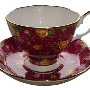 May include: A vintage teacup and saucer set. The cup and saucer feature a burgundy background with a floral pattern of yellow and pink roses. The rims are trimmed with gold.