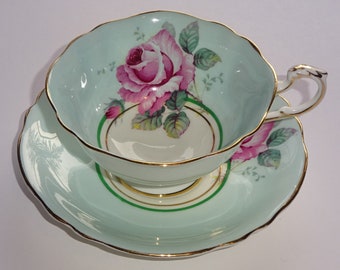 May include: A light blue teacup and saucer set with a pink rose design and gold trim.
