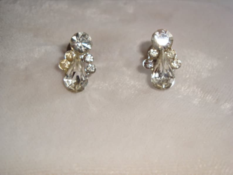 Puede incluir: Un par de pendientes de tono plateado con piedras de cristal transparente en forma de l&aacute;grima y cristales transparentes m&aacute;s peque&ntilde;os que rodean las piedras m&aacute;s grandes.