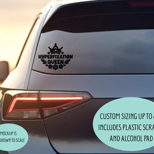 May include: A black vinyl car decal featuring a crown icon above the text HYPERFIXATION QUEEN, surrounded by floral and heart motifs. The decal is displayed on a car window. Text on the image indicates custom sizing up to 6x6 inches.