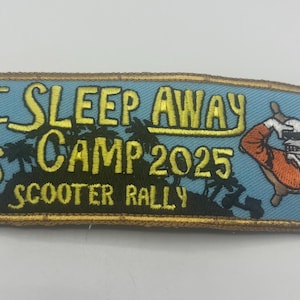 May include: Embroidered patch with the text "IT SLEEP AWAY CAMP 2025 SCOOTER RALLY" in yellow lettering on a light blue background. A cartoon character in an orange shirt and sunglasses is on the right. The patch has a gold border.