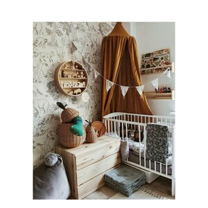 May include: A child's nursery with a white cot, wooden storage, and a round wooden shelf. The room has a mustard-coloured canopy and black and white animal wallpaper. There are soft toys and a grey beanbag. The room is decorated with bunting.